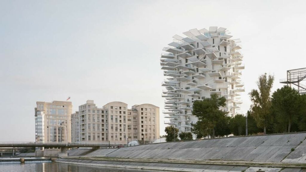 tour blanche aux balcons superposés face au canal, immeubles et arbres en arrière-plan.